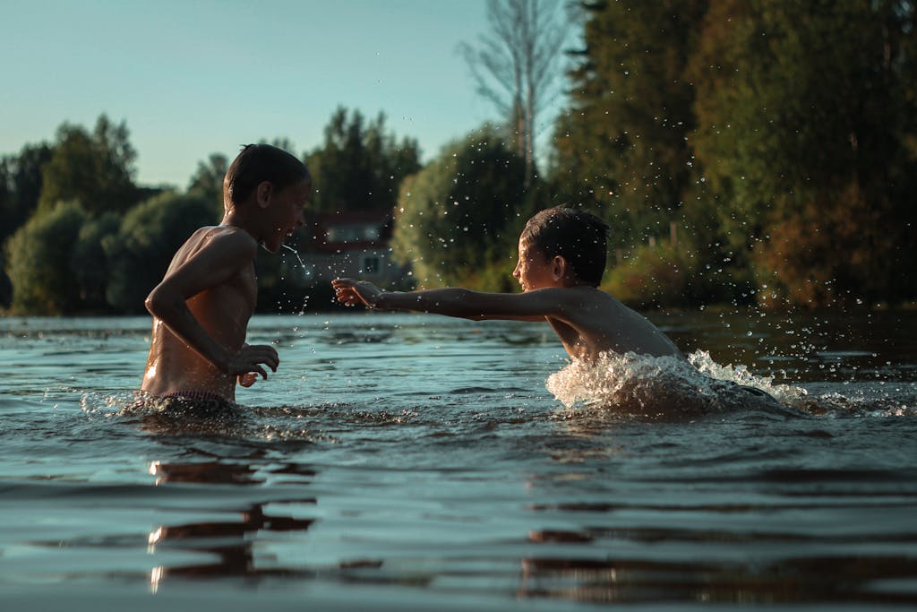 Two boys enjoy a playful splash in the tranquil outdoors, embracing the joy of summer by the water.